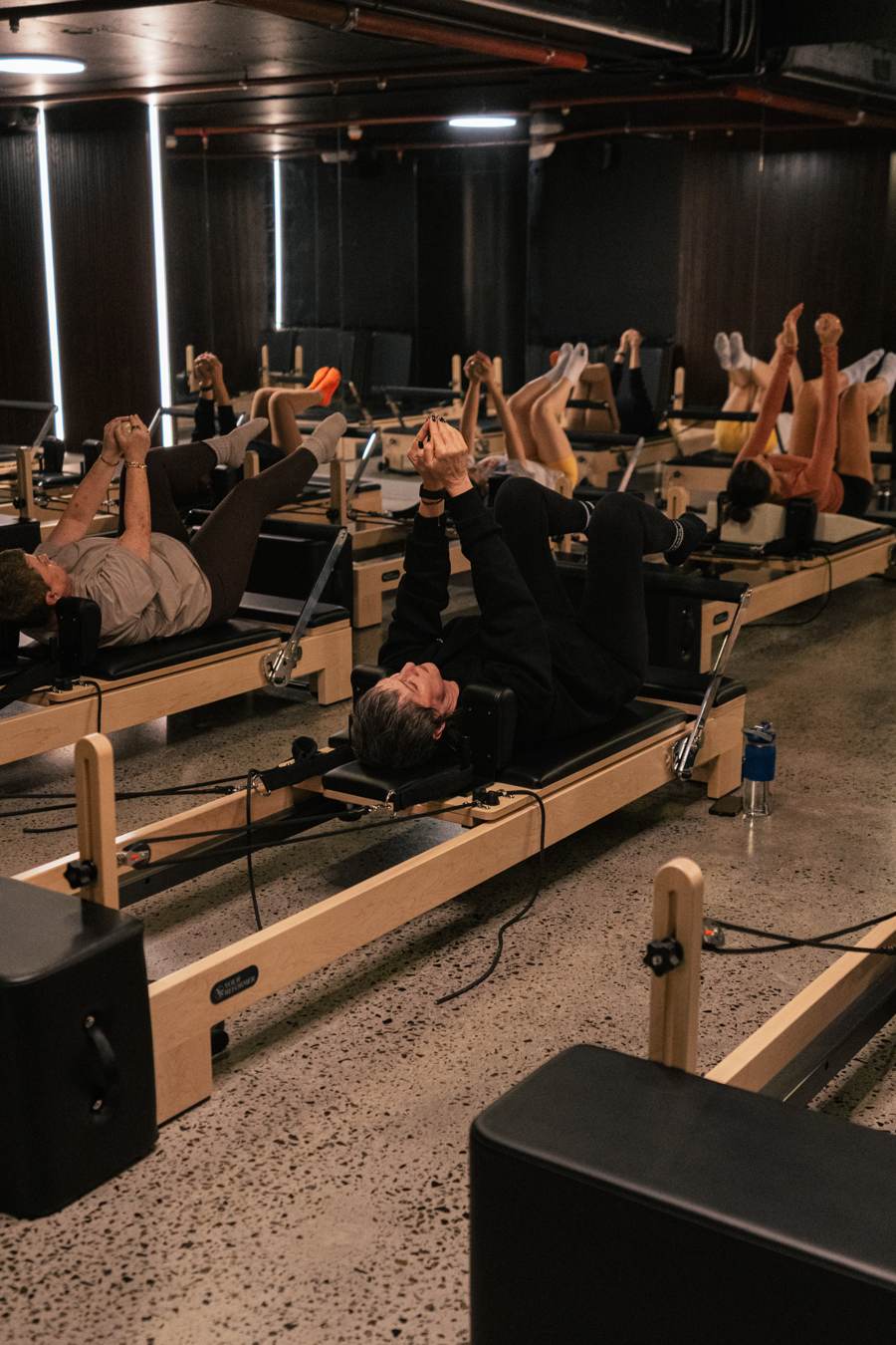 A full reformer class at 4ME Pilates, members mid-movement with legs raised.